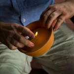 Person using a lighter to light a potted citronella candle to keep mosquitoes away.