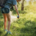 Person in tall grass applying mosquito spray to their legs