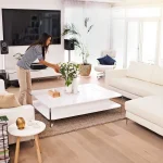 A woman decluttering and tidying up a bright modern living room to prepare her home for professional bed bug treatment.