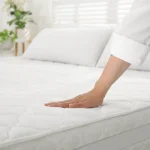 A person's hand smoothing down a clean, bare white mattress with a quilted cover after taking steps to get rid of bed bugs.