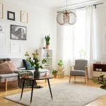 A well-lit, modern apartment living room decorated with a grey sofa, wooden furniture, and potted plants.